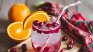A refreshing beverage in a clear glass, garnished with fresh cranberries and a slice of orange
