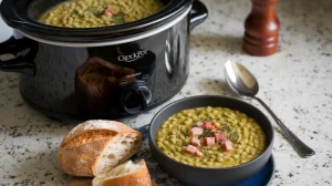A black ceramic Crock-Pot slow cooker of mushy split pea soup, placed on a white granite countertop