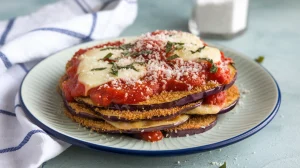 A plate of eggplant parmesan. The layers consist of breaded and fried eggplant slices, topped with a a red marinara sauce, grated parmesan and mozzarella