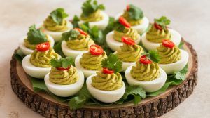 a wooden platter filled with green curry deviled eggs topped with a cilantro leaf