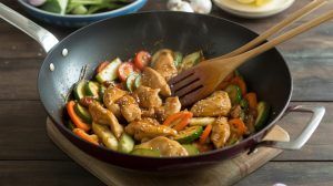 chicken pieces and sliced vegetables in a wok with a wooden fork stirring