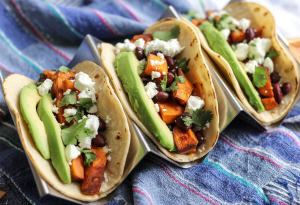 three gourmet tacos made with soft corn tortillas filled with roasted sweet potatoes, black beans, and topped with fresh avocado slices