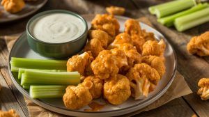 a platter of crispy buffalo cauliflower bites with celery sticks and a small bowl of blue cheese dressing