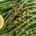 a plate of fresh green beans almondine seasoned with black pepper and fresh garlic and served with lemon slices