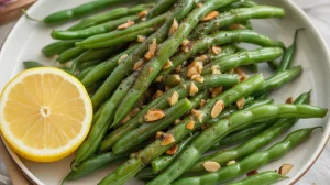 a plate of fresh green beans almondine seasoned with black pepper and fresh garlic and served with lemon slices