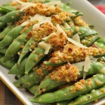 a platter of freshly roasted snap peas topped with fresh garlic, panko breadcrumbs, and fresh grated parmesan
