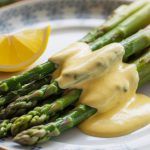 a plate of asparagus topped with hollandaise sauce