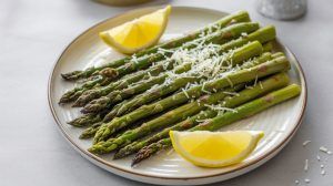 a plate of roasted asparagus topped with grated parmesan cheese and 2 lemon wedges
