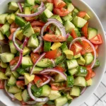 A vibrant summer salad consisting of diced cucumbers, diced avocado chunks, chopped red tomatoes, thinly sliced red onions, and fresh dill scattered throughout
