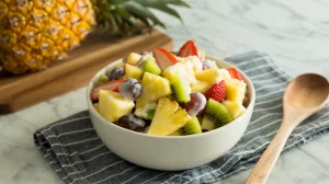 A vibrant fruit salad in a white ceramic bowl placed on a gray and white striped cloth napkin.
