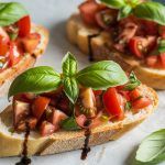 toasted Italian bruschetta on a platter topped with diced tomato chunks, fresh basil leaves, and topped with a drizzle of balsamic vinegar