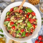 a Mediterranean-style quinoa salad in a white ceramic bowl with a wooden spoon