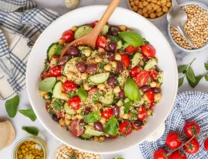 a Mediterranean-style quinoa salad in a white ceramic bowl with a wooden spoon