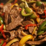 beef steak fajitas in a sizzling skillet with sliced onion and bell peppers