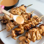 grilled chicken skewers on a white ceramic plate. The chicken pieces are glazed and charred with grill marks, arranged in a circular pattern