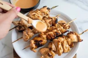 grilled chicken skewers on a white ceramic plate. The chicken pieces are glazed and charred with grill marks, arranged in a circular pattern
